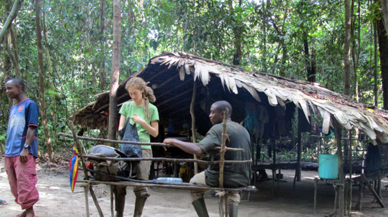 Selbst gebaut: Die Biologin und zwei Mitarbeiter vor der Küche ihres Camps. Foto: Vera Leinert Vera Leinert steht vor einer Hütte im Wald, die aus Stöcken gebaut ist und ein Blätterdach trägt.