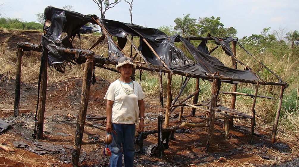 Damiana, ein Guaraní-Kaiowá und religiöse Führerin der Apyka'y, vor einer niedergebrannten Hütte nach Zwangsvertreibungen Guarani-Kaiowá vor zerstörter Hütte