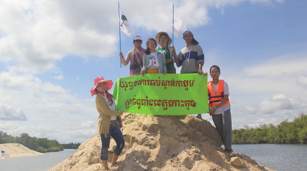 „Stoppt den Sandabbau in der Provinz Koh Kong“, fordern die Umweltschützer von Mother Nature Umweltschützer stehen auf einem aufgeschütteten Sandhügel und halten ein Protestbanner hoch: Kampagne gegen Sandabbau in der ganzen Koh Kong-Provinz