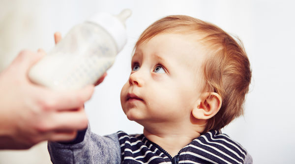 Ein Baby wehrt mit sorgenvollem Blick eine ihm hingehaltene Trinkflasche ab