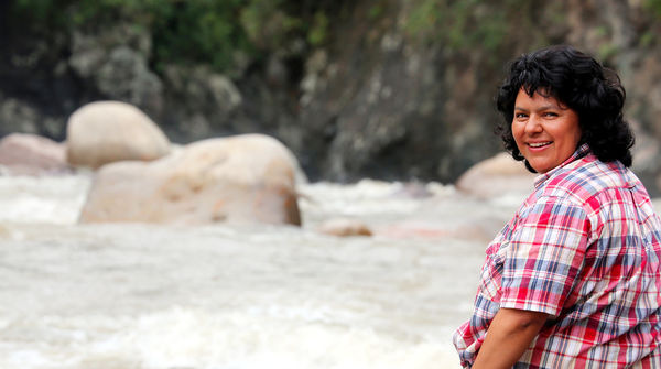 Die Umweltaktivistin Berta Cáceres sitzt auf einem Stein am Fluss und blickt über ihre Schulter in die Kamera